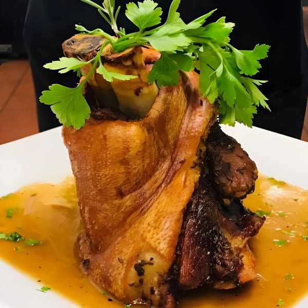 Crispy roasted pork shank, or Schweinshaxe, garnished with fresh parsley and served in a rich gravy.