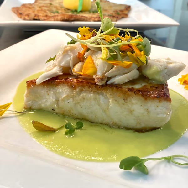 Pan-seared fish with crab meat, microgreens, and edible flowers on a green sauce.