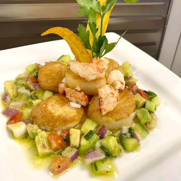 Pan-seared scallops and lobster with avocado, cucumber, and tomato salsa, garnished with plantain and parsley.